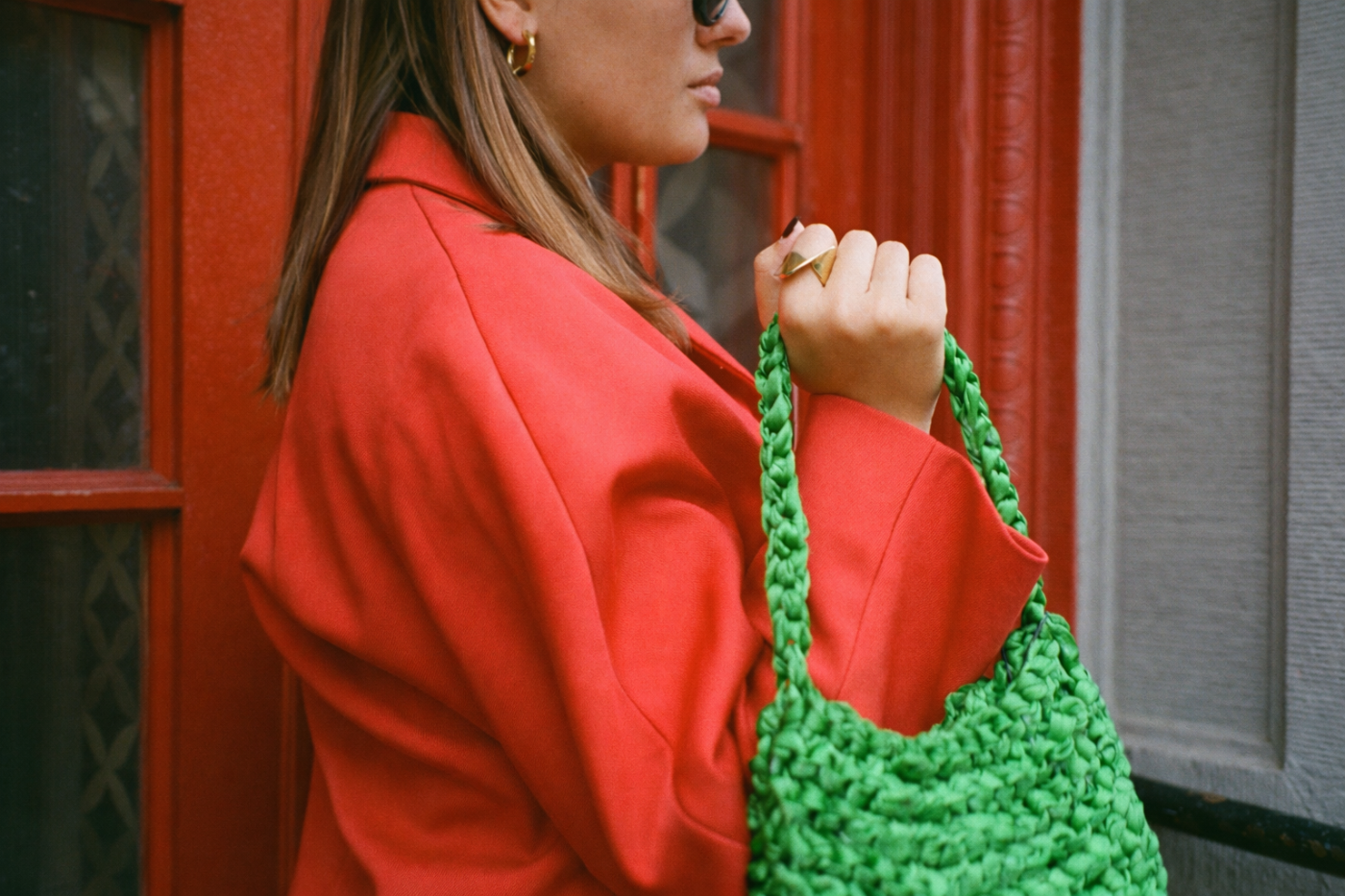 Woman in a red coat holding a green knitted bag against a red door wearing Brydie Ring
