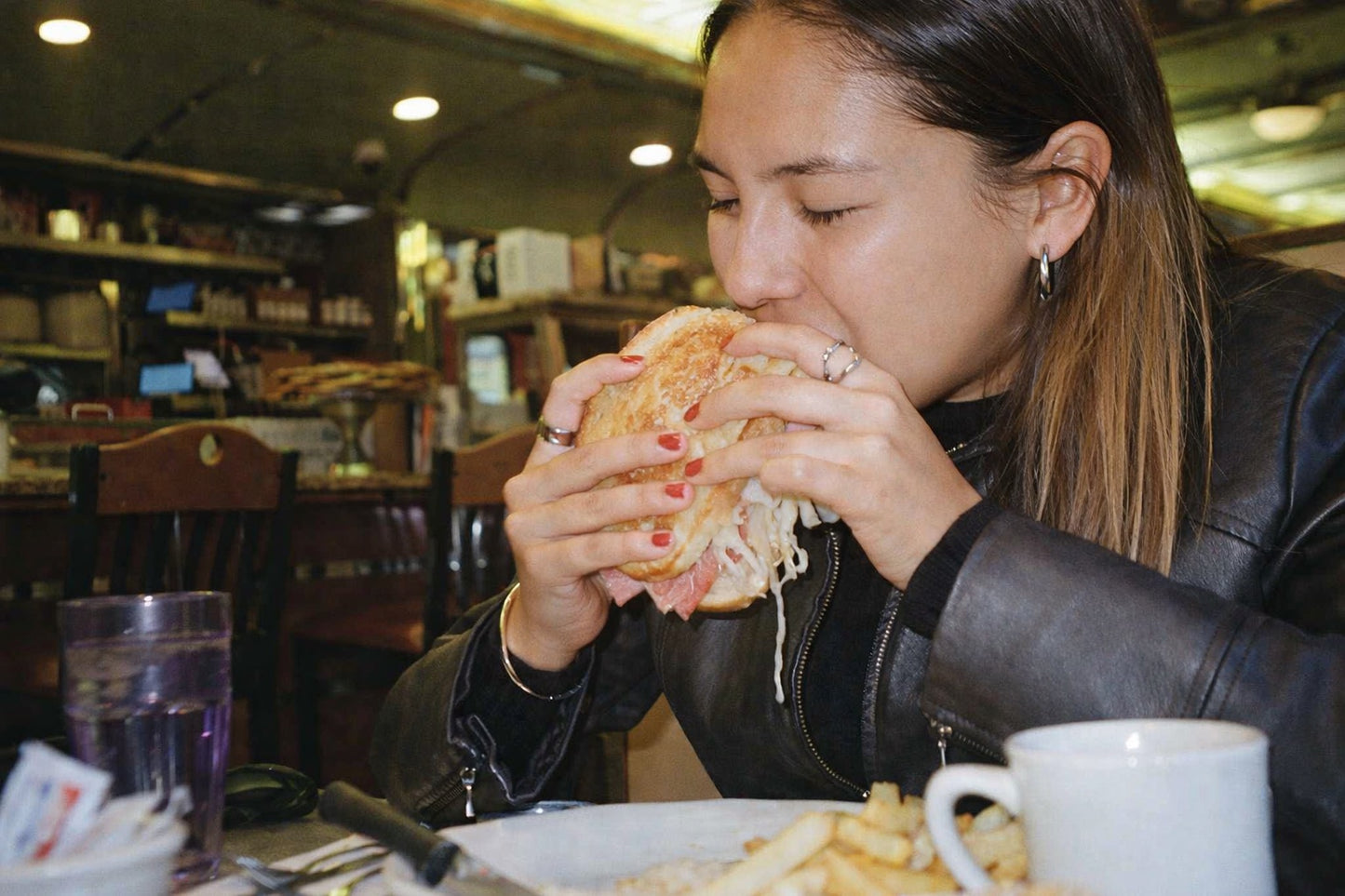 Woman eating a sandwich in a New York City diner setting wearing the Genevieve Ring
