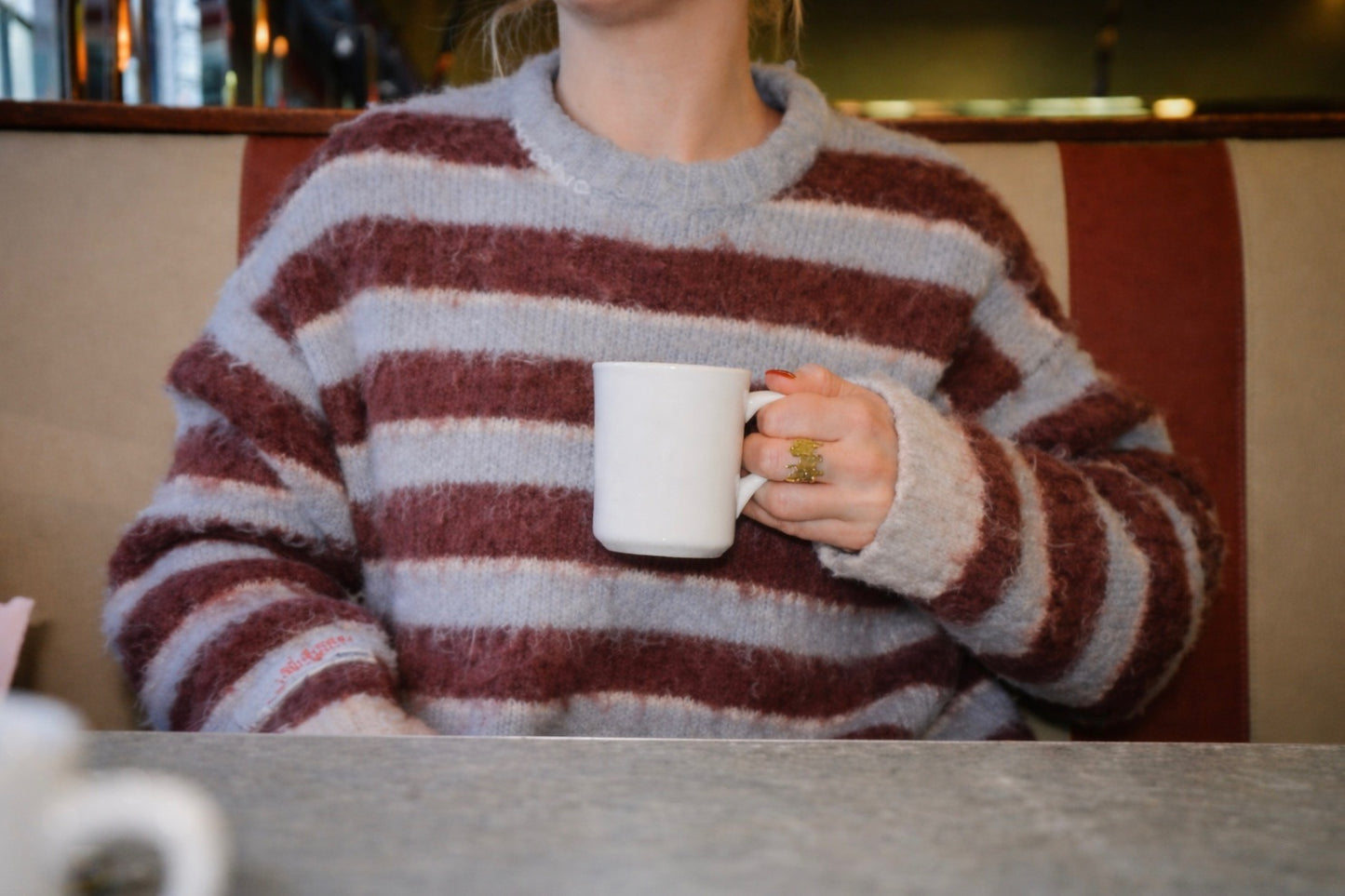 Person wearing a striped sweater holding a white mug in a casual setting