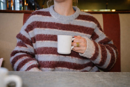 Person wearing a striped sweater holding a white mug in a casual setting
