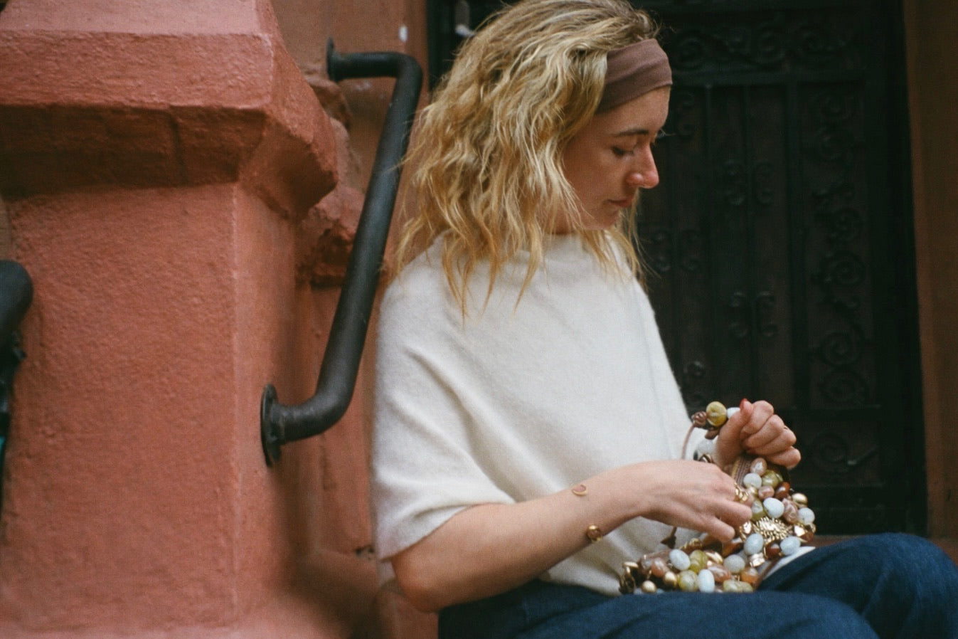 Woman sitting on a bench with a textured wall and black railing in the background wearing madison cuff and roshe ring