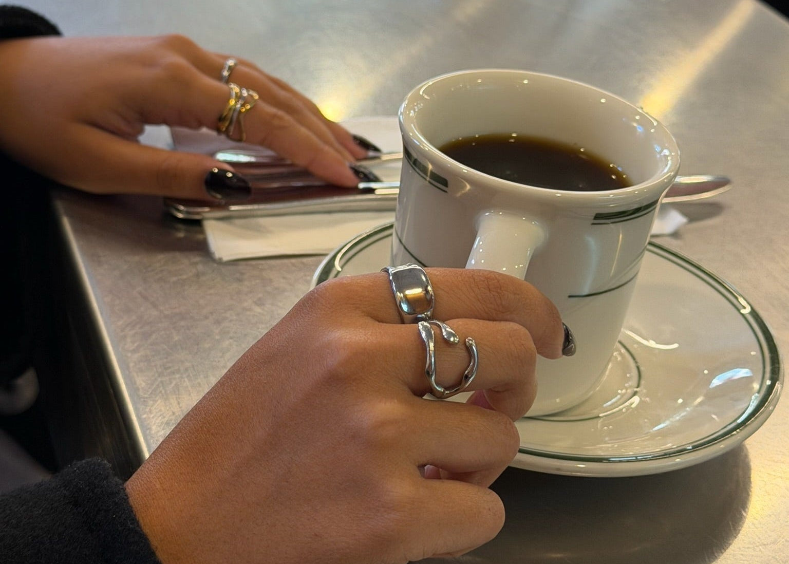 Person holding a white coffee cup with a ring on a metal surface