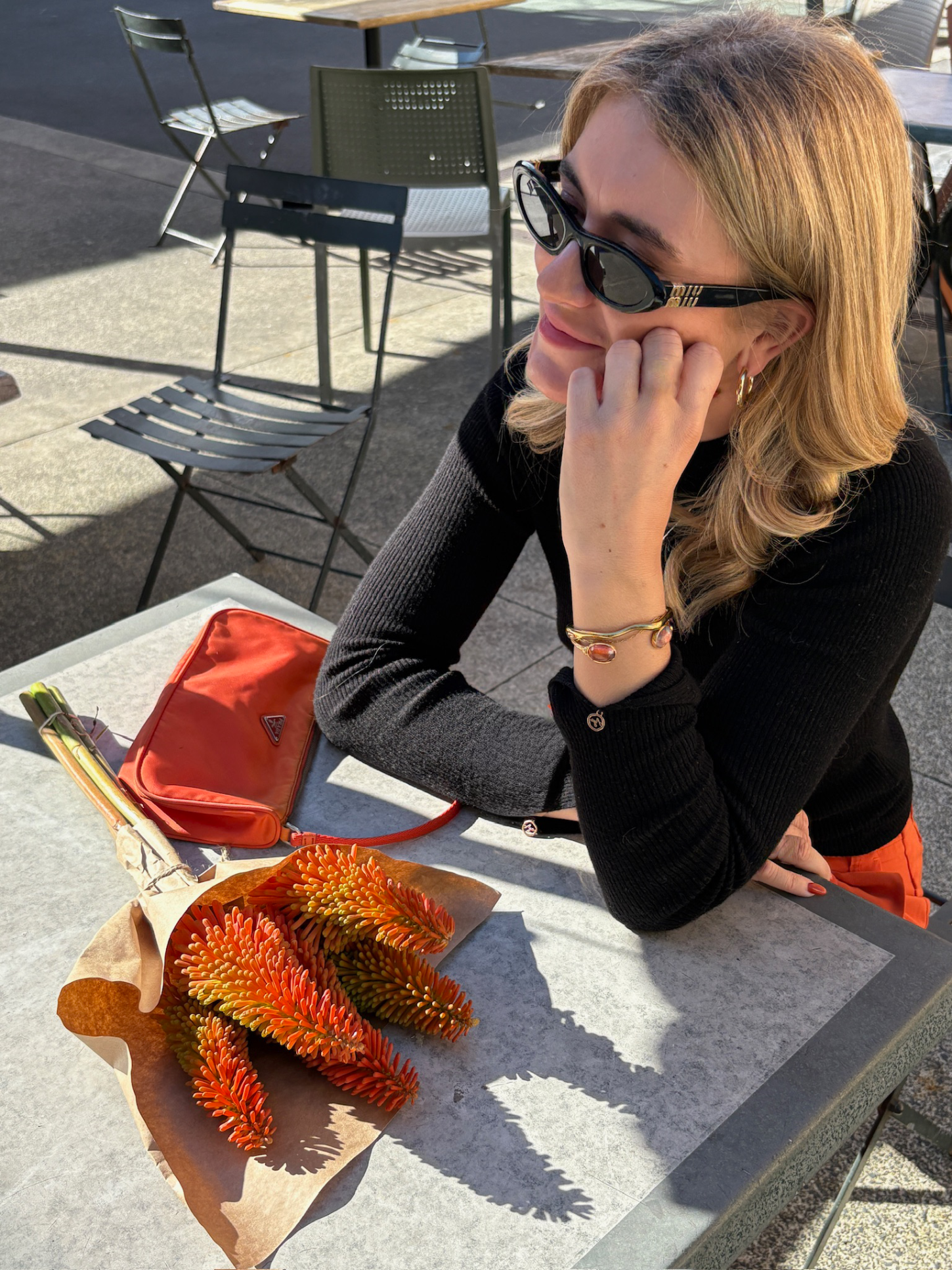 Woman sitting at an outdoor table with a bouquet of flowers and an orange handbag wearing the Madison Cuff - Burnt Orane