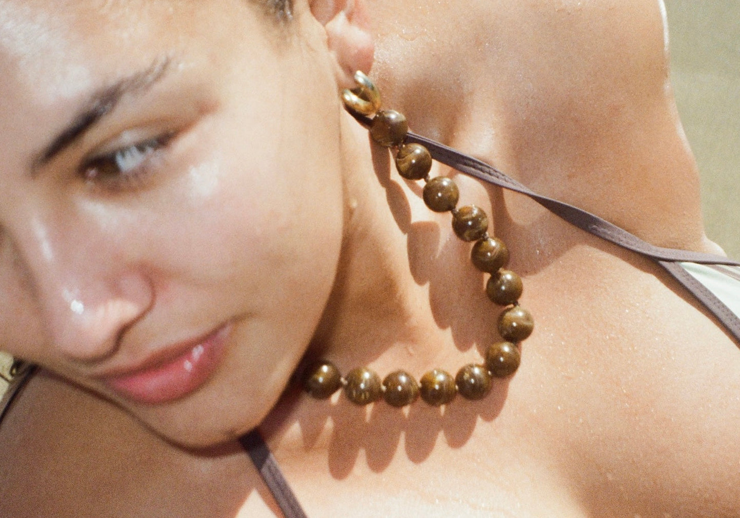 A close-up lifestyle shot of a woman wearing a chunky beaded necklace and matching large drop earrings made of brown tiger's eye beads.