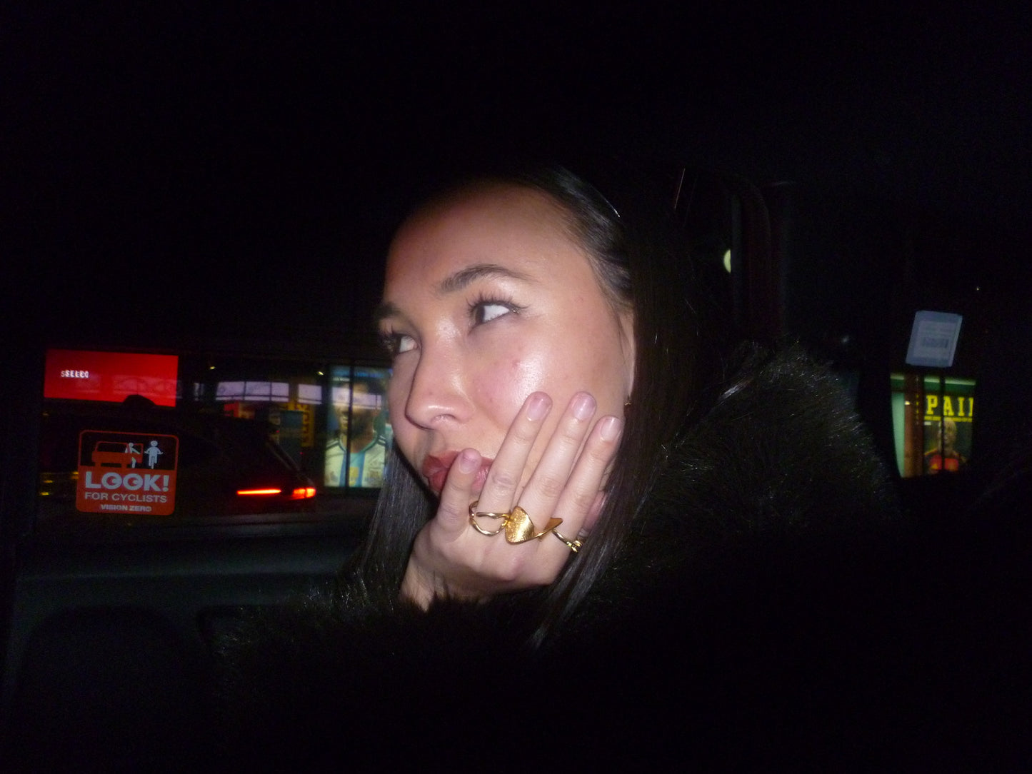 Woman with a ring on her finger in a dark setting with blurred lights in the background. Brydie Ring, New York City