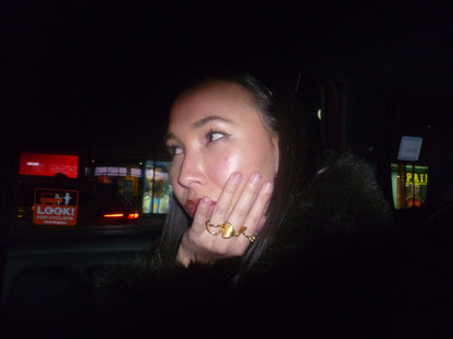 Woman with a ring on her finger in a dark setting with blurred lights in the background. Brydie Ring, New York City